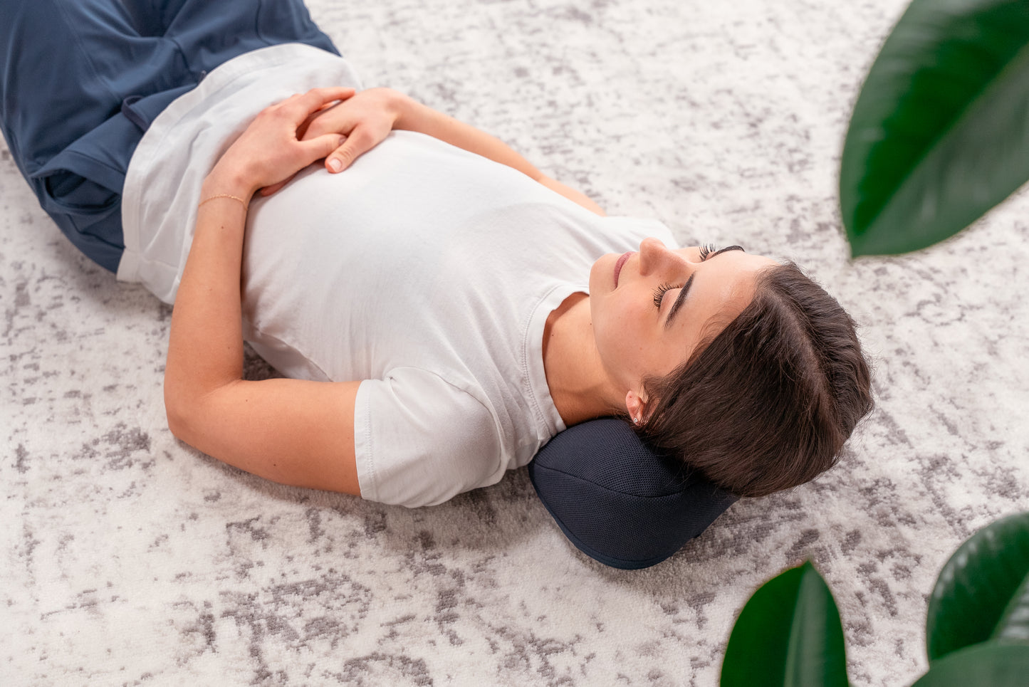 Overhead view of Side view of female model using the HALO Neck Stretch Pillow while lying on the floor.