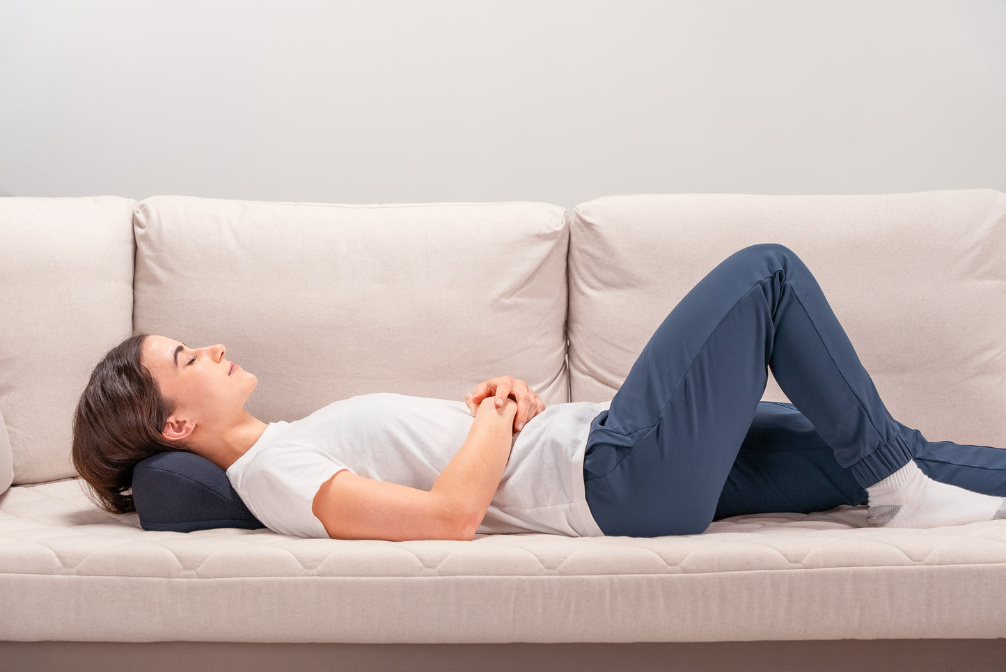 Side view of female model using the HALO Neck Stretch Pillow while lying on sofa.